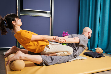 Masseuse making thai yoga massage. Woman therapist doing traditional massage treatment, stretching...