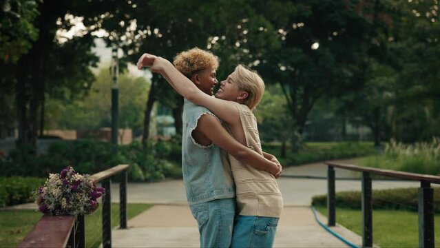 Affectionate gay partners kiss and hug standing on bridge in green urban park. Young homosexual men show love on romantic date in city garden. LGBT community pride month celebration