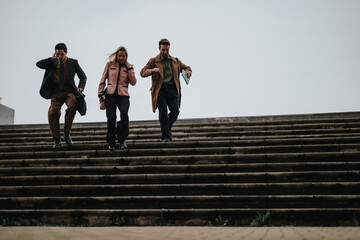 Fototapeta premium Three business professionals in smart casual attire descending outdoor steps together, embodying teamwork and determination.