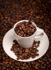 Espresso cup filled with roasted coffee beans, coffee bean background.
