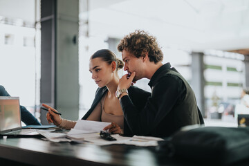 Young professionals working together in the office, discussing project details using a laptop and documents. Focused and collaborative work environment.