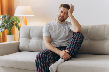 Young man suffering from headache at home, touching his temples, copy space, blurred background....
