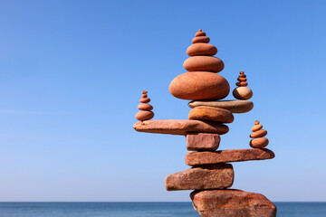 A large rock zen pyramid made of red balanced stones against a background of sea and blue sky