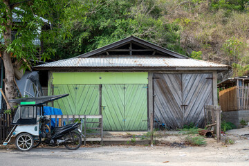 Bentor or becak motor, a motorized vehicle like a rickshaw, is parked in front of an old wooden house