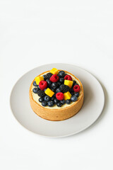 Cheesecake decorated with fresh berries and mango. On a light gray plate. White background. Back view. There is a copy space for your text.
