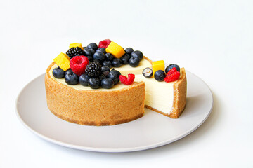 Slice cheesecake decorated with fresh berries and mango. On a light gray plate. White background. Back view. There is a copy space for your text.