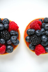 French dessert. Three berry tarts are decorated with organic fresh blueberries, raspberries and blackberries. White background. Top view. 