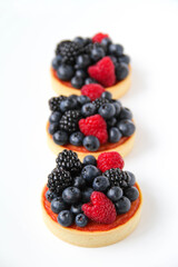 French dessert. Three berry tarts are decorated with organic fresh blueberries, raspberries and blackberries. White background. Back view. 
