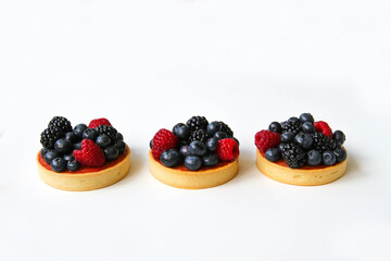 French dessert. Three berry tarts are decorated with organic fresh blueberries, raspberries and blackberries. White background. Back view. 
