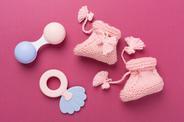 Pink baby booties and rattles on color background, top view