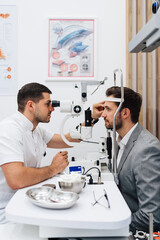 Fototapeta premium Attractive male doctor ophthalmologist is checking the eye vision of handsome middle age man in modern clinic. Doctor and patient during medical check up in ophthalmology clinic.