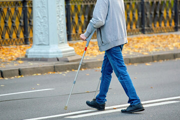 Man crossing the road on crutches, violation of pedestrian safety rules in an urban environment. Man with crutches navigating road crossing, violation of pedestrian safety regulations..