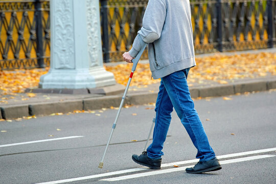 Man crossing the road on crutches, violation of pedestrian safety rules in an urban environment. Man with crutches navigating road crossing, violation of pedestrian safety regulations..