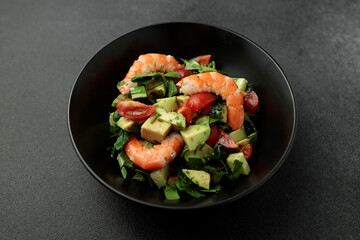 Salad of king prawns, avocado, cucumber, tomato and herbs. Black background