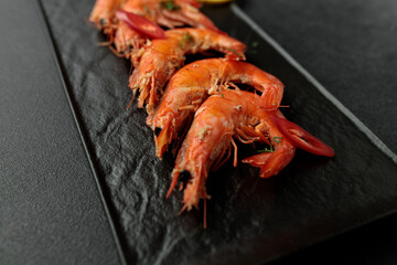 Large cooked king prawns on a black background. Lemon slices