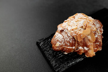 Almond croissant. puff pastry, delicate frangipane cream with almonds, enriched with butter. On top, the croissant has a hint of almond flakes and powdered sugar. on a black cutting board