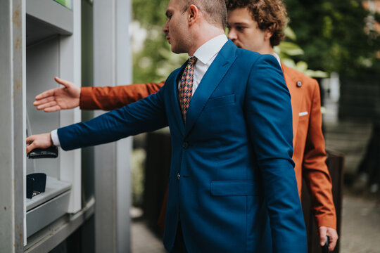 Two businessmen in formal attire encounter an issue with an ATM withdrawal, showcasing a problem while using the machine outdoors.