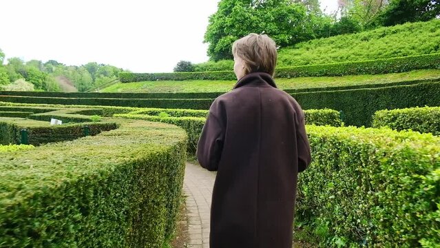 A solitary figure walks through a maze of tall, green hedges, following the winding path