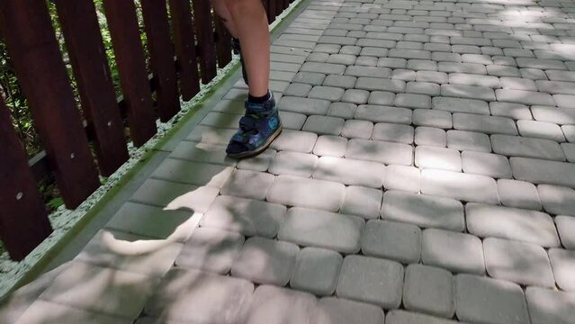 Unrecognizable legs of a child with movement coordination problems walking along a path in the park. cerebral palsy
