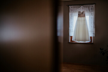 A beautifully captured wedding dress hanging in a room, showcasing its intricate design and elegance against a serene backdrop