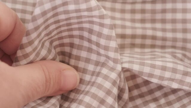 Female hands inspecting texture and quality checkered cotton fabric, testing for durability, stretch and crease resistance textile material