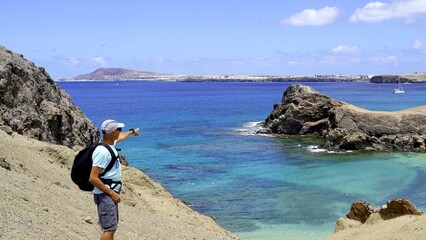 Man points with finger overseas at the lava rock coast of the volcanic Canary Islands. The man is a...