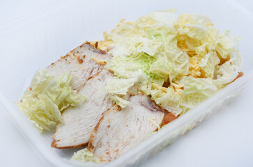 Caesar salad with meat and vegetables in a plastic container. A light breakfast.
