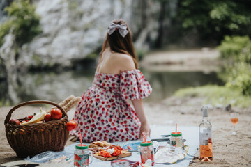 Woman having a peaceful picnic in nature by a river. Basket of fruits and beverages create a relaxing outdoor atmosphere.