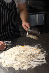 A man chef in an apron prepares pasta in a restaurant kitchen. Kneads the dough with eggs. The process of preparing pasta dough. Noodles. Italian Cuisine. Recipe.
