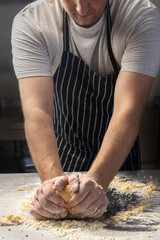 A man chef in an apron prepares pasta in a restaurant kitchen. Kneads the dough with eggs. The process of preparing pasta dough. Noodles. Italian Cuisine. Recipe.