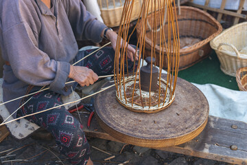 An elderly woman weaves a basket by hand.