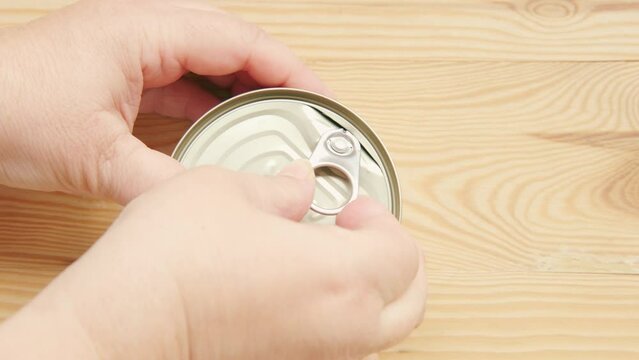 caucasian hands opens tin can on wooden board surface, opening with ring-pull opener, Independent living skills, Everyday kitchen essentials, everyday task preparing food at home