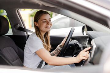 Young woman adjusting car radio while driving modern vehicle