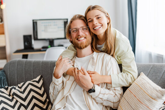 Young couple is hugging and smiling on sofa at home looking at camera