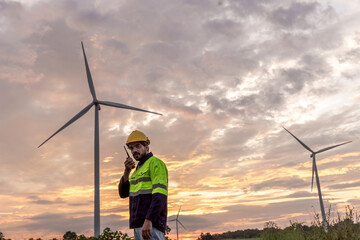 Professional Man Maintenance engineers working in wind turbine farm at sunset.  Engineer Man standing among Wind Energy Turbine.