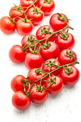 Group of ripe cherry tomatoes on branches, on a white wood textured background.