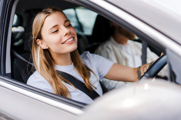 Young woman smiling while driving her car with boyfriend in passenger seat