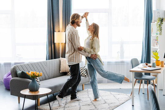 Happy young couple is dancing at home in the living room - Powered by Adobe