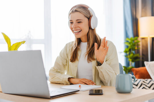 Smiling young woman with headphones waving during video call at home office
