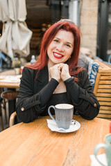 Beautiful happy woman with long red hair enjoying coffee in a street cafe