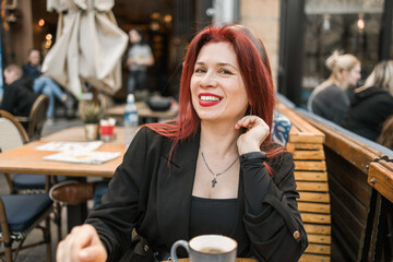 Beautiful happy millennial woman with long red hair enjoying day in a street cafe copy space