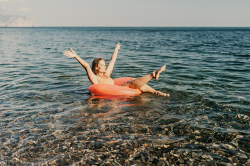 A woman is floating in a red inflatable tube in the ocean