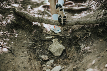 Close-up view of a hiker's shoes navigating a forest trail, stepping over a tree root. Captured during daytime in a natural setting.