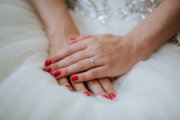 A close-up of a bride's hands gently clasped together, highlighting the intricate details of her wedding dress and the delicate jewelry adorning her wrists.