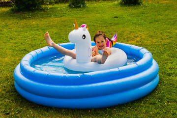 Little girl child swims in the pool on an inflatable unicorn-shaped toy on a summer day outdoors.