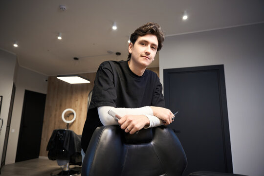 Experienced barber posing at camera in contemporary hairdressing salon