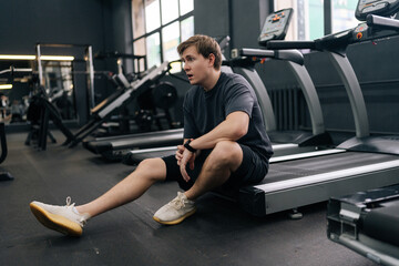 Portrait of tired runner taking break at sport gym sit on treadmill. Portrait of exhausted sweaty...