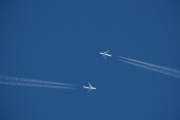 Two airplanes in the blue sky with contrails