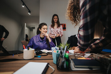 A group of diverse colleagues collaboratively work at a cluttered office desk, actively discussing business strategies and solution development in a vibrant workplace environment.