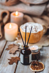 Autumn home perfume in glass bottle with wooden sticks, scented candles as apartment air freshener. Pumpkin sweet latte fragrance, spices, cinnamon, anise. Aromatherapy, cozy atmosphere, comfort